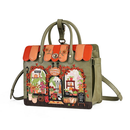 An olive green tote bag with a detailed autumn-themed storefront patchwork design on the front, featuring orange awnings, floral arches, pumpkins, and a 'Happy Fall Wink' sign, shown on a white background.
