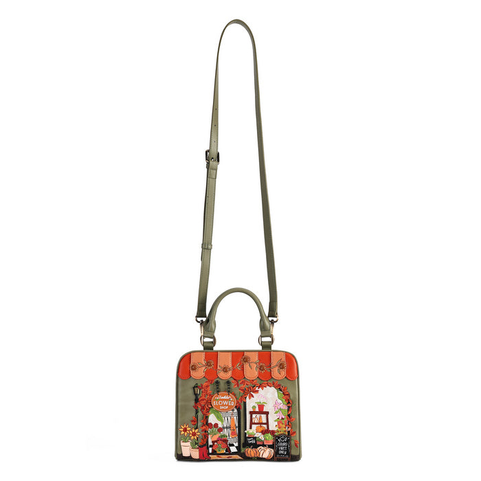 A small rectangular shoulder bag with a long olive green strap and top handle, featuring a colorful illustrated front panel with a vintage storefront scene and red-orange striped accents, shown on a plain white background.