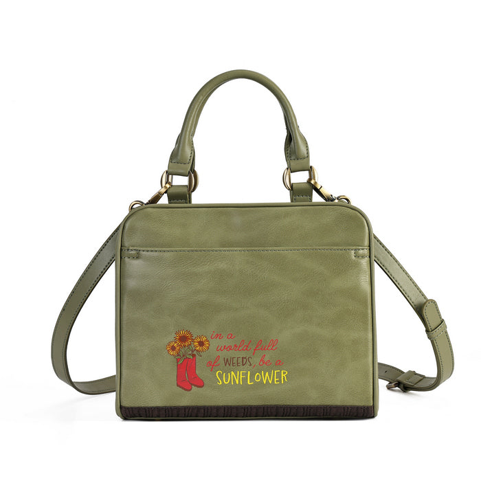 An olive green faux-leather handbag with a top handle, adjustable shoulder strap, and a front pocket featuring a red and yellow embroidered design with the text 'there is plenty of weeds but she is a SUNFLOWER' and a red boot holding sunflowers.