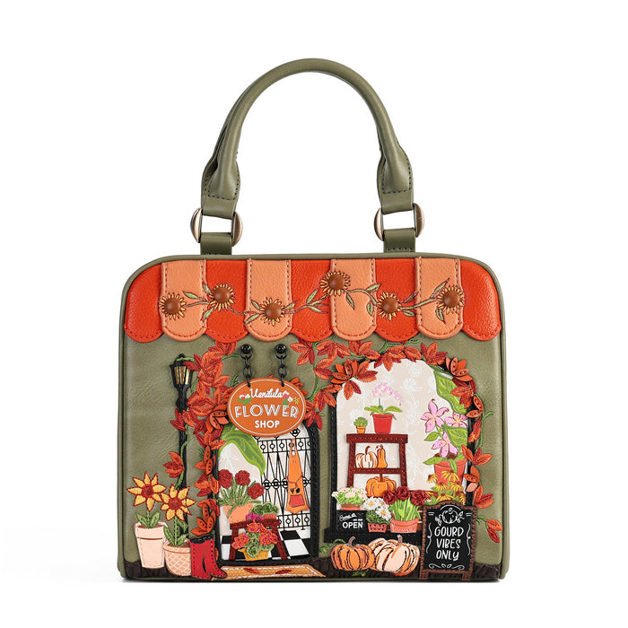 An olive green structured handbag with a top handle, featuring a detailed embroidered autumn flower shop scene on the front. The design includes orange awnings, red leaves, pumpkins, flowers, and a 'Floralde's Flower Shop' sign, set against a plain white background.