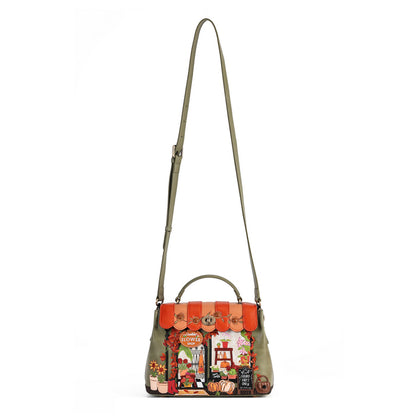 An olive green leather shoulder bag with a top handle and a long adjustable strap, featuring a highly detailed, colorful storefront illustration on the front flap.