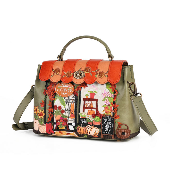 An olive green handbag with a top handle and shoulder strap, featuring a detailed autumn-themed embroidered design of a flower shop on the front flap, complete with pumpkins, flowers, and a scalloped orange trim.