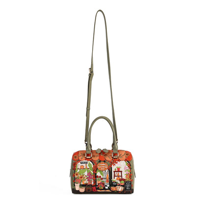 A structured handbag with a long olive green shoulder strap and double top handles, featuring a colorful, busy collage-style print on the front panel with autumn and kitchen motifs.
