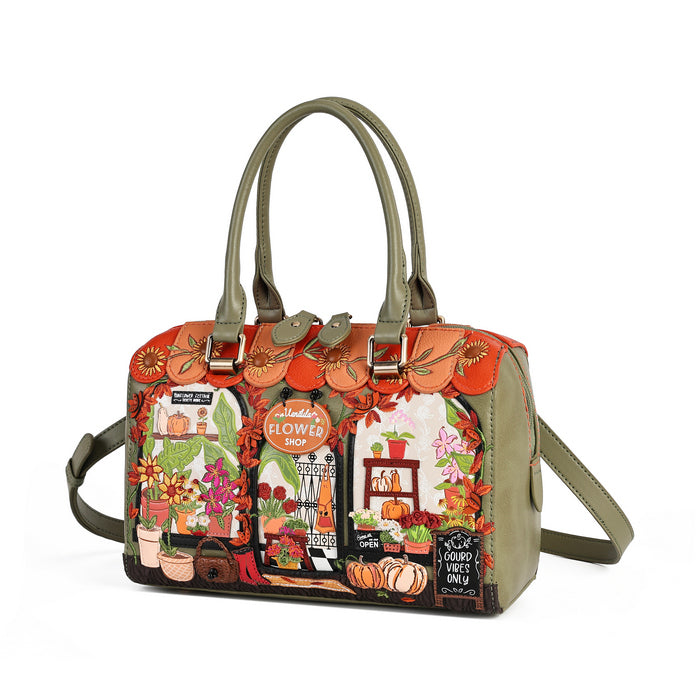 A structured handbag with olive green handles and shoulder strap, featuring a colorful autumn-themed illustration on the front depicting a flower shop, pumpkins, and orange leaves.