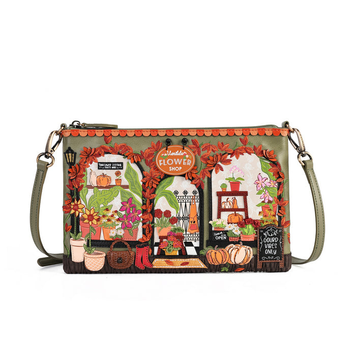 A rectangular shoulder bag with a green base and an intricate autumn-themed illustration of a flower shop window. The design features orange fall leaves, potted flowers, pumpkins, and a chalkboard sign, with a matching green strap and gold-tone hardware.