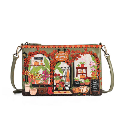 A rectangular shoulder bag with a green base and an intricate autumn-themed illustration of a flower shop window. The design features orange fall leaves, potted flowers, pumpkins, and a chalkboard sign, with a matching green strap and gold-tone hardware.