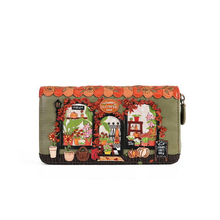 A rectangular zip-around clutch wallet featuring a detailed, colorful illustration of a flower shop facade on an olive green background, with orange scalloped trim and autumn-themed details.