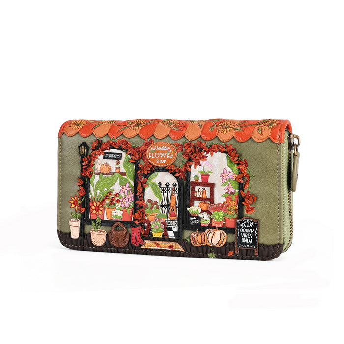 An olive green zip-around clutch wallet featuring a highly detailed, colorful embroidered design of a flower shop with autumn decorations, displayed on a clean white background.