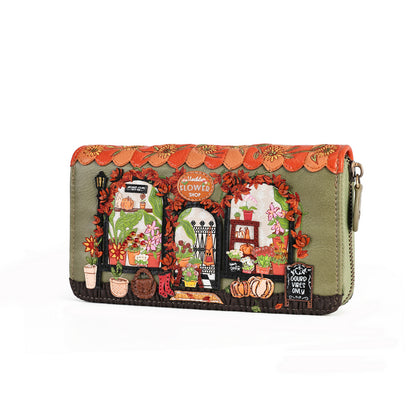 An olive green zip-around clutch wallet featuring a highly detailed, colorful embroidered design of a flower shop with autumn decorations, displayed on a clean white background.