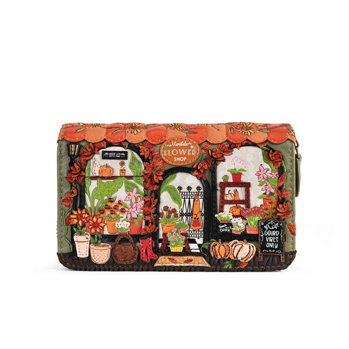 A rectangular zip-around clutch bag featuring a highly detailed, colorful embroidered design of a flower shop storefront with autumn elements like pumpkins, flowers, and a scalloped orange roof, shown against a plain white background.