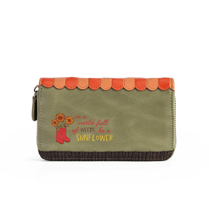 An olive green zip-around wallet with a scalloped orange and peach trim along the top, a dark brown stitched bottom edge, and embroidered text reading 'in a world full of weeds, be a sunflower' with sunflowers and red boots.