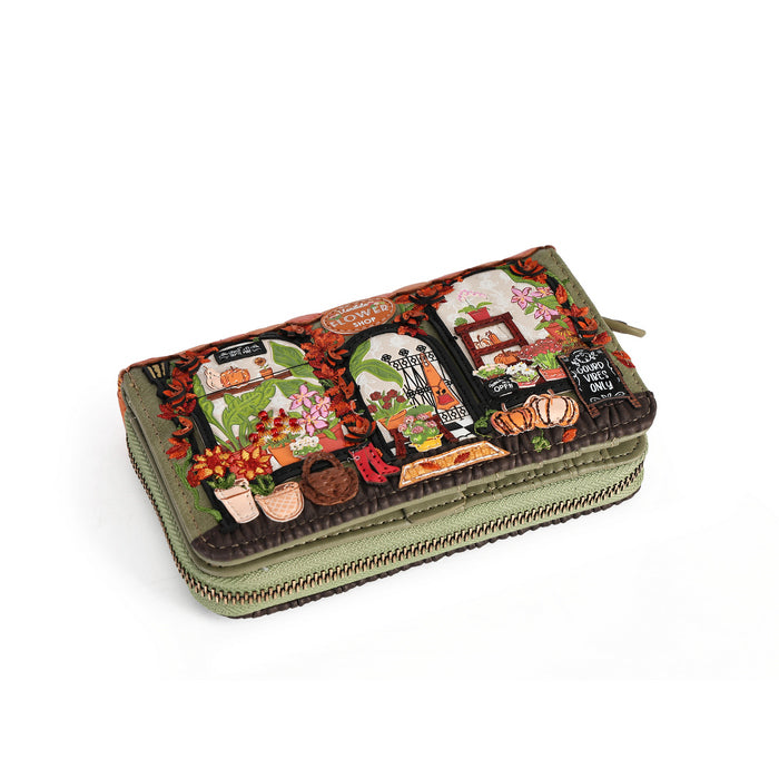 An olive green zip-around wallet with a highly detailed, colorful autumn-themed patchwork design on the front, featuring fall leaves, pumpkins, flowers, and vintage storefronts, shown on a plain white background.
