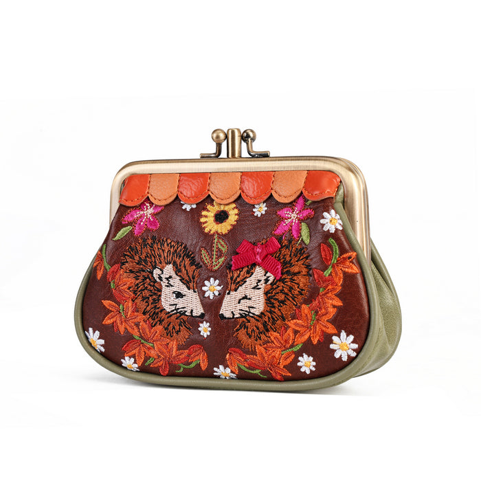 A kiss-lock purse with a brown leather body, featuring embroidered hedgehogs, orange autumn leaves, white daisies, and pink flowers, with a gold-tone metal frame.