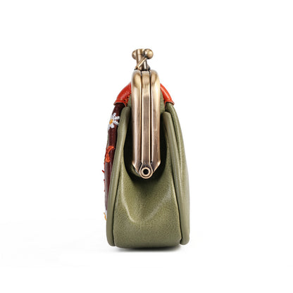 A close-up side view of a green leather handbag with a brass kiss-lock clasp and a red embroidered fabric accent on a white background.