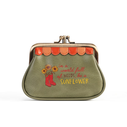 An olive green faux leather kiss-lock coin purse with a scalloped orange and brown trim, featuring a red rain boot and sunflower graphic with the text 'in a world of weeds, be a SUNFLOWER' in red and yellow lettering.