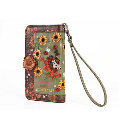 A vertical zip-around wallet with a wrist strap, decorated with a woodland hedgehog illustration, sunflowers, red ladybugs, and the words 'The Wild Flowers of the Weedle Sunflower'.