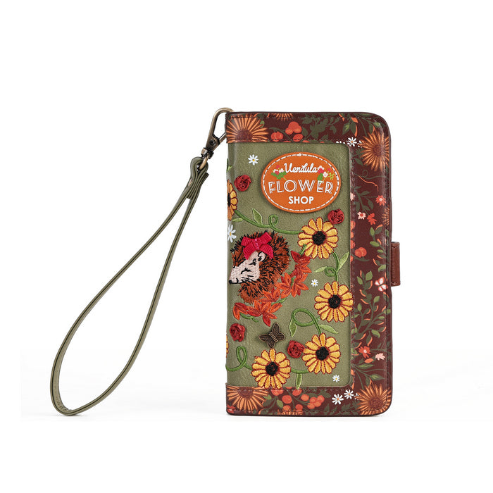 A floral wallet phone case with a wrist strap, featuring a green center panel with a hedgehog, yellow flowers, and a brown patterned border, complete with an oval 'Hedgehog's Flower Shop' logo patch.