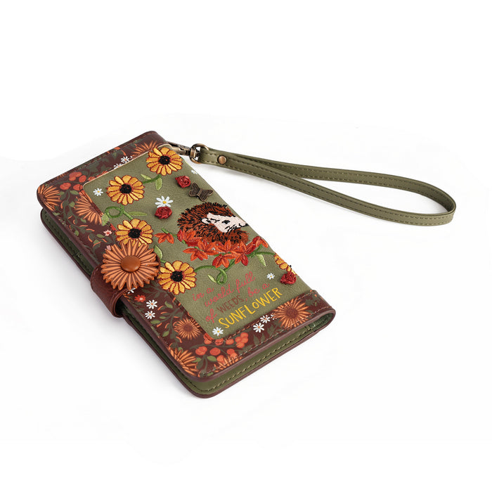 A wallet-style phone case with an olive green wrist strap, decorated with a rustic sunflower and floral pattern in orange, brown, and green, featuring the text 'Just a little SUNFLOWER' on a white background.