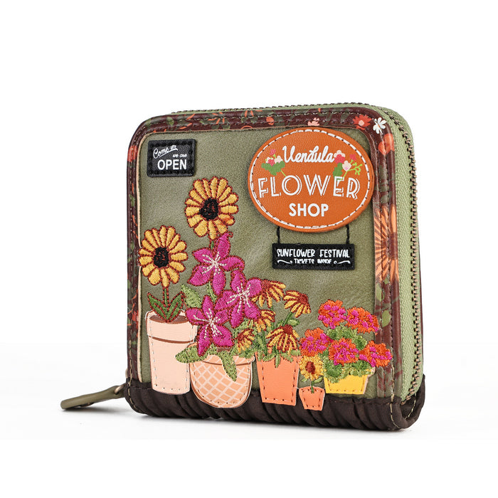A small zip-around coin purse with a vintage-style floral patchwork design. The front features embroidered and printed flowers in pink, yellow, and orange pots on an olive green background, with decorative labels including 'Ventura Flower Shop' and 'Sunflower Festival'.