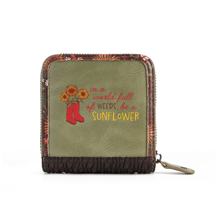 An olive green zip-around wallet with a floral patterned border, a dark brown gathered bottom, and embroidered text reading 'in a world full of weeds, be a SUNFLOWER' alongside red boots and yellow sunflowers.
