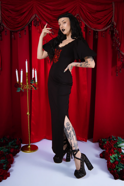 Woman in a black outfit posing in front of red curtains with candles and floral decorations.