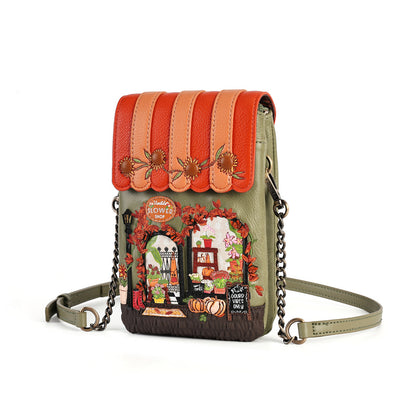 A small crossbody bag with a green base and a decorative autumn-themed front panel. The flap has orange and peach vertical stripes with three brown deer appliqués, and the front features a colorful embroidered storefront scene with pumpkins, fall leaves, and seasonal motifs.