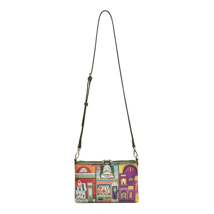 A small crossbody bag with a colorful, whimsical storefront pattern in red, yellow, green, and purple, featuring an olive green shoulder strap and gold-tone hardware, shown against a plain white background.