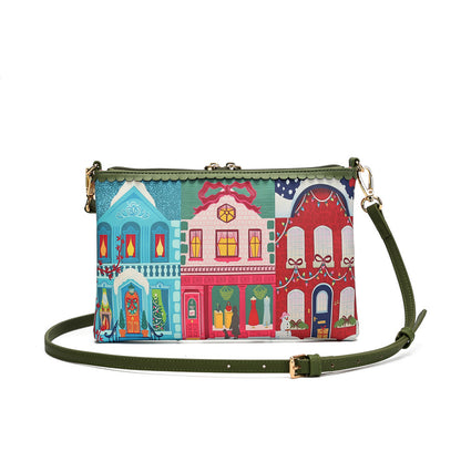 A small crossbody clutch bag with an olive green strap and a colorful printed design of three stylized storefront buildings in blue, pink, and red, shown on a plain white background.