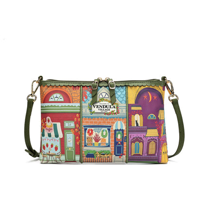 A rectangular shoulder bag with an all-over colorful architectural storefront print, olive green trim and strap, and a central metal plaque reading Vendula Village.