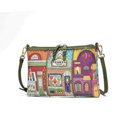 A multicolor crossbody bag featuring a vibrant, whimsical storefront illustration pattern. The bag has an olive green strap, gold-tone hardware, and a central metal plaque that reads 'VENDULA VILLAGE'.