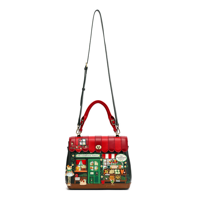 A structured handbag with a red top handle and a long black shoulder strap, featuring a colorful illustrated storefront design on the front and a red scalloped trim along the top.