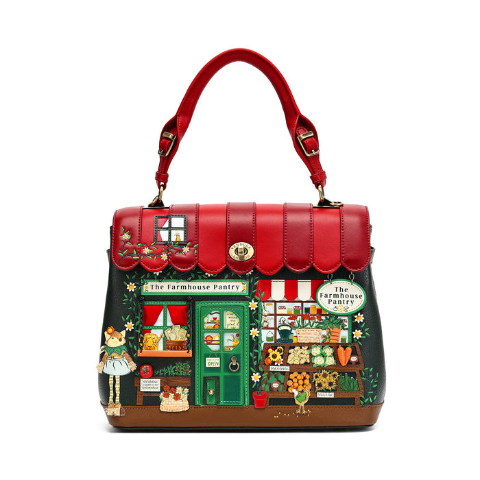 A handbag designed to look like 'The Farmhouse Pantry' from Alice in Wonderland, featuring a red top handle, a dark green body, and a highly detailed, colorful illustration of the bakery storefront with characters and produce.