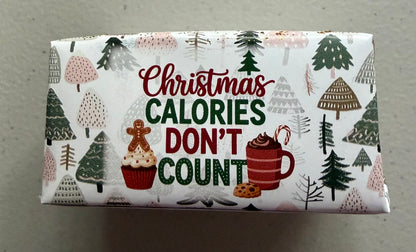 A wrapped candy bar featuring a festive Christmas design with the text 'Christmas CALORIES DON'T COUNT' in red and green lettering, surrounded by illustrations of pine trees, a gingerbread man, a cupcake, and a mug of hot chocolate on a white background.