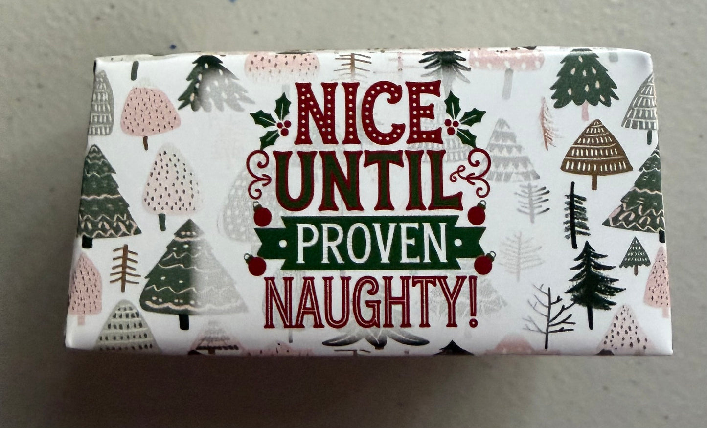 A rectangular box of Christmas-themed soap or lotion with a white background and festive pattern. The front features the text 'NICE UNTIL PROVEN NAUGHTY!' in red and green lettering, surrounded by illustrated pine trees and holly leaves.