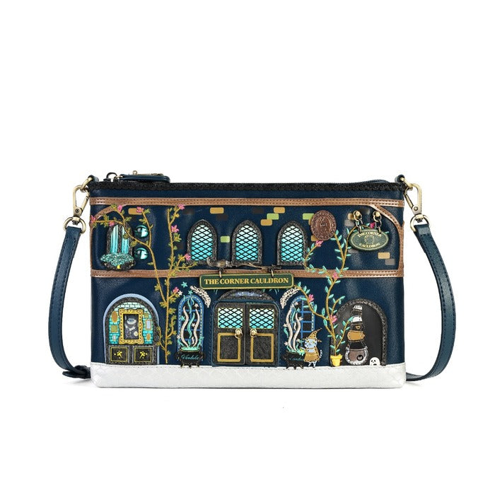 A navy blue crossbody clutch bag featuring an embroidered depiction of 'The Corner Calicoons' storefront. The bag has a navy blue leather strap, gold-tone hardware, and a white base trim, with detailed multicolor embroidery showing windows, flowers, and animals.
