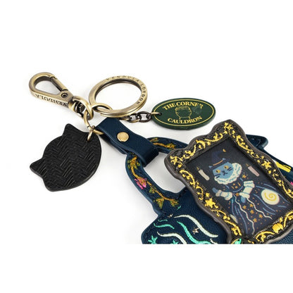 A decorative keychain set featuring a black textured cat-shaped charm, a gold-toned lobster clasp and split ring, a green oval tag reading 'THE CORNE'S CAULDRON', and a navy blue fabric charm with gold trim and a blue cauldron illustration.