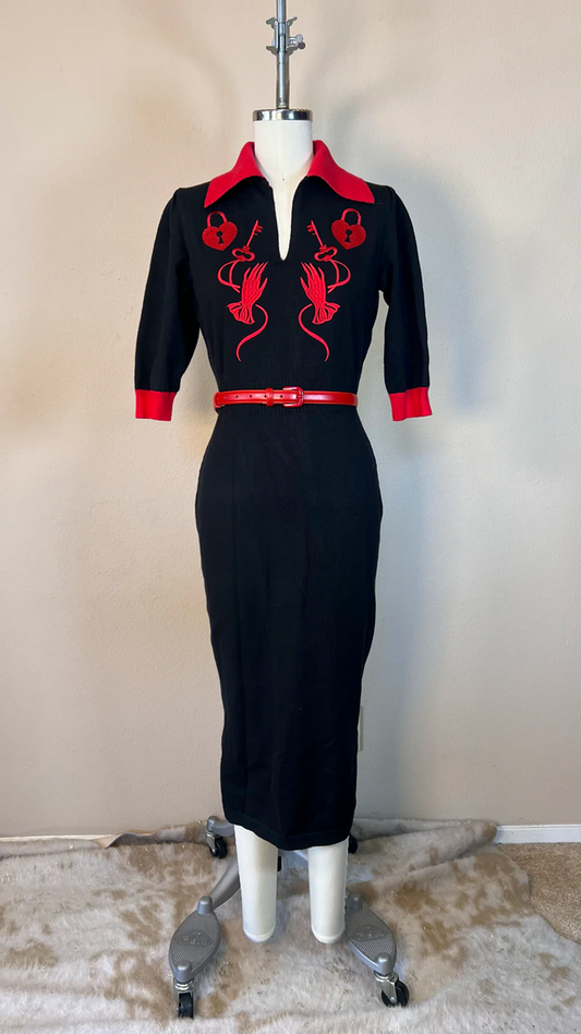 Black dress with red accents on a mannequin against a beige wall.