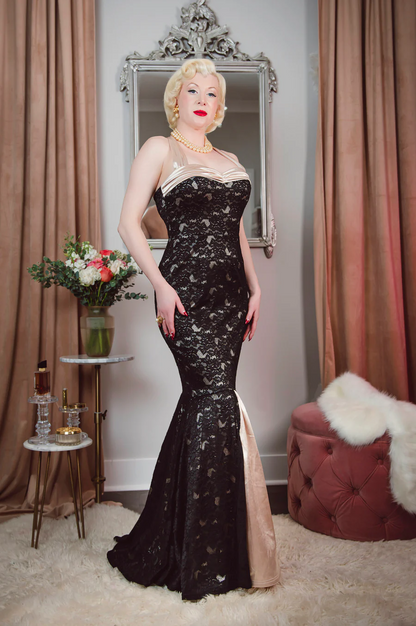 Woman in a black sequined evening gown standing in a room with curtains and a mirror.