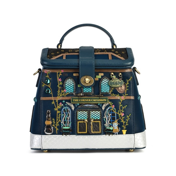 A navy blue handbag designed to look like a whimsical house facade, featuring embroidered details, a gold-tone snap closure, and a silver textured base, shown on a plain white background.