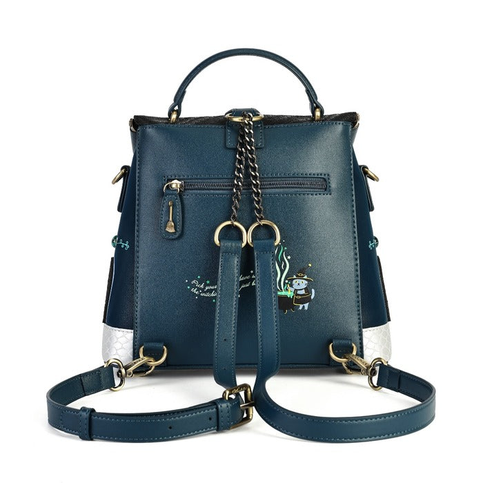 A dark teal blue leather backpack with gold-tone hardware, featuring a top handle, a detachable shoulder strap, a front zip pocket, and a small embroidered cartoon character on the lower right side.