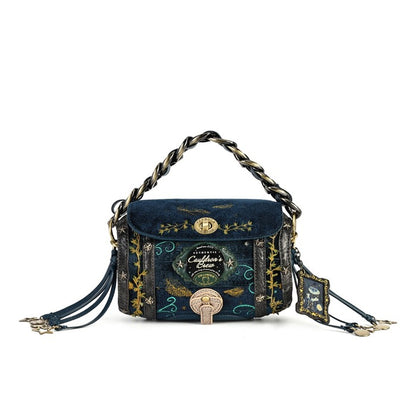A dark blue velvet and patterned fabric handbag with gold and black decorative details, a braided top handle, and tassel straps, shown on a plain white background.