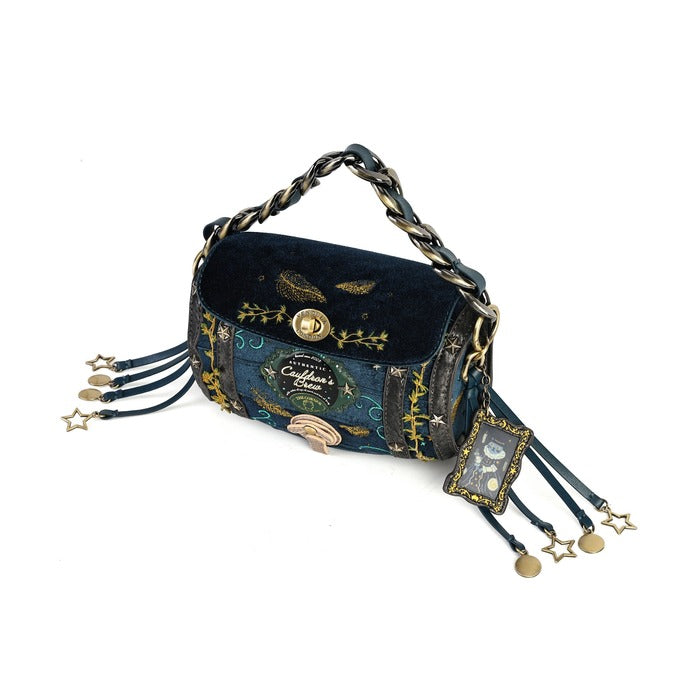 A dark blue velvet and patterned fabric shoulder bag with gold-toned hardware, a chain strap, and dangling star charms on a white background.