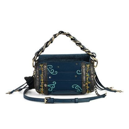 A navy blue denim crossbody bag with gold and turquoise embroidery, featuring a chunky chain handle, a detachable leather strap, and tassel details, shown against a plain white background.