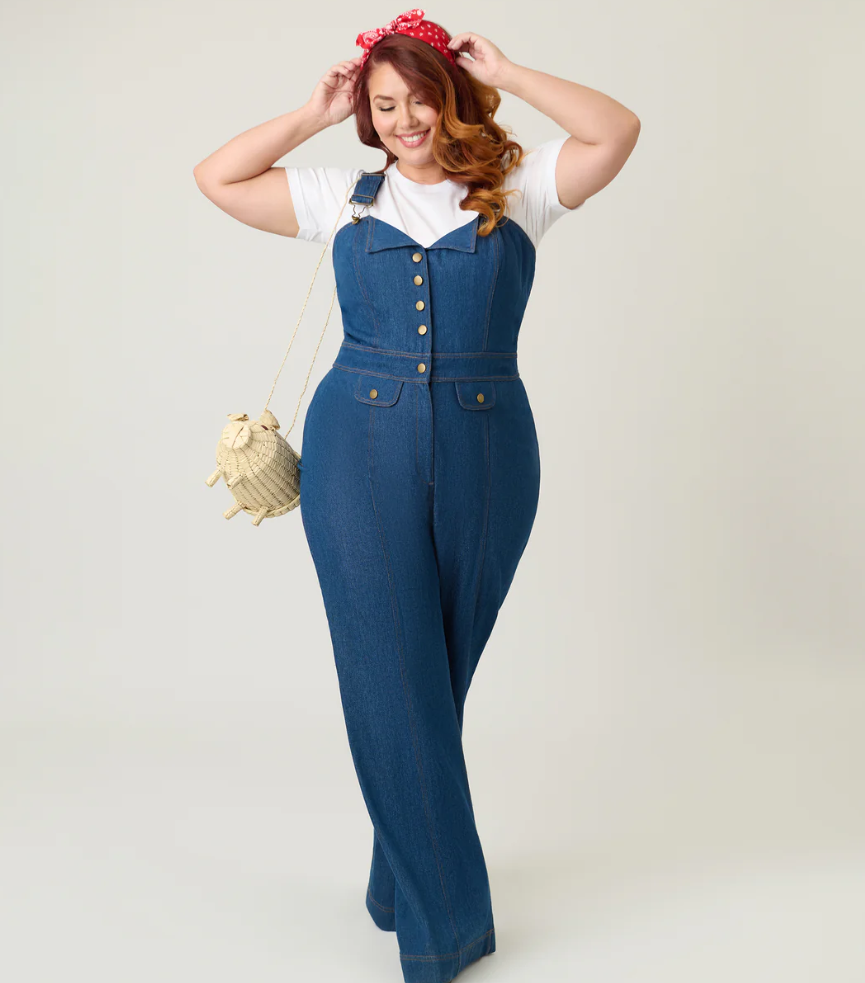 Woman wearing a blue denim jumpsuit with a white shirt underneath, posing against a plain background.
