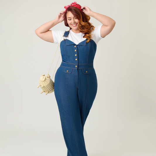 Woman wearing a blue denim jumpsuit with a white top, posing against a plain background.