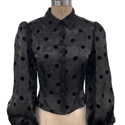 A black sheer long-sleeve blouse with black polka dots, featuring a Peter Pan collar and puffed balloon sleeves, displayed on a beige mannequin torso against a white background.