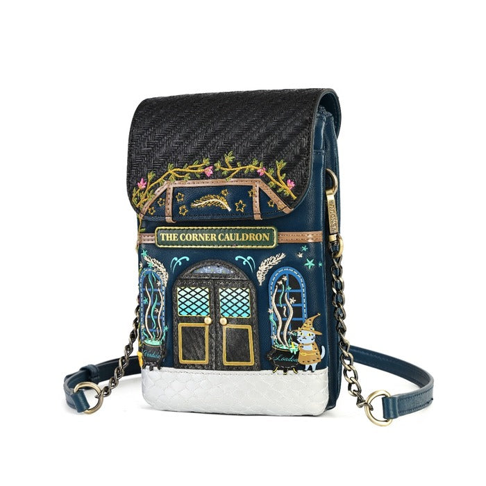 A small crossbody bag with a dark navy blue and black woven flap, featuring an embroidered 'The Corner Cauldron' design with gold, teal, and pink details, a white quilted base, and a gold chain strap on a white background.