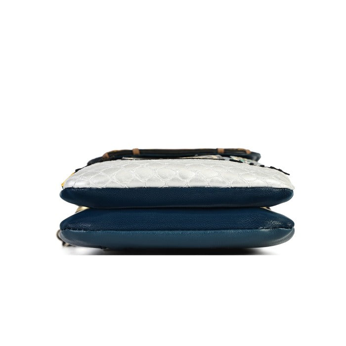 A close-up of a handbag's bottom section, featuring navy blue leather, a white textured python skin panel, and a dark brown bamboo handle, shown against a plain white background.