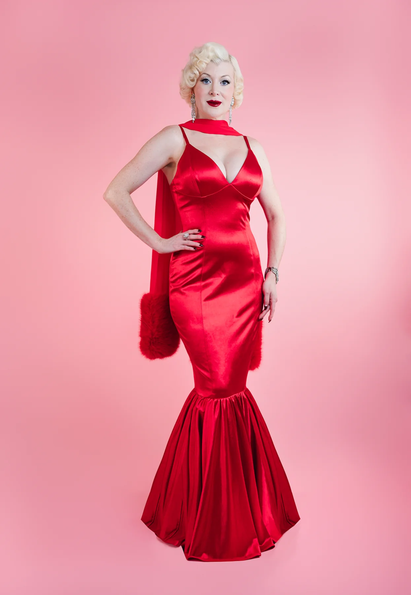 Woman in a red dress posing against a pink background