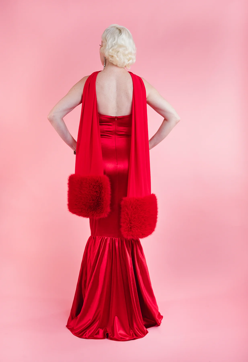 Woman wearing a red evening gown with fur accents on a pink background